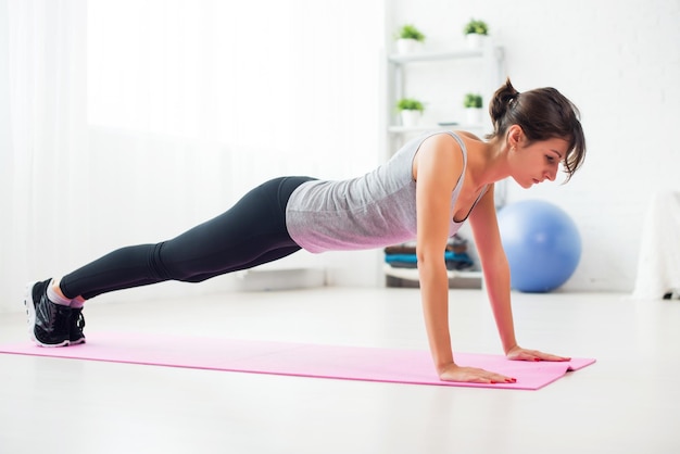 Fitte Frau macht Liegestütze auf dem Boden in ihrem Wohnzimmer und zu Hause eine Trainingsmatte