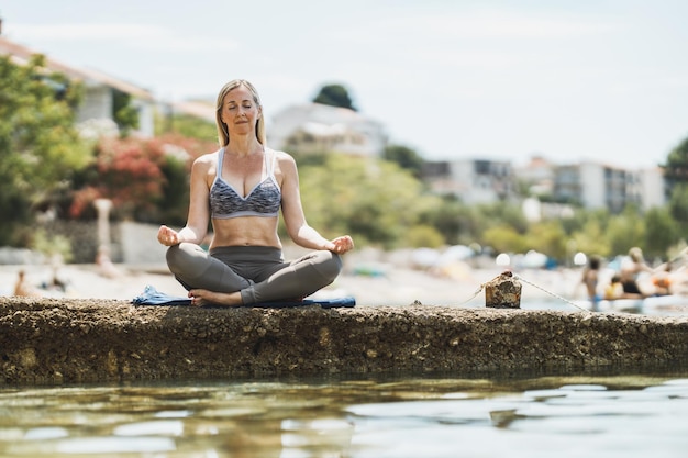 Fitte Frau mittleren Alters, die während des Trainings in der Nähe des Meeresstrandes Yoga-Übungen macht.