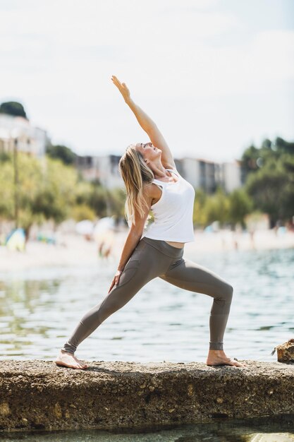 Fitte Frau mittleren Alters, die während des Trainings in der Nähe des Meeresstrandes Yoga-Übungen macht.