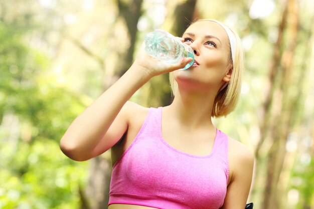 fitte Frau trinkt Wasser im Wald beim Joggen