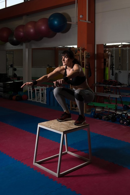 Fitte junge Frau beim Boxspringen in einem Fitnessstudio. Sportlerin führt Boxsprünge im Fitnessstudio durch