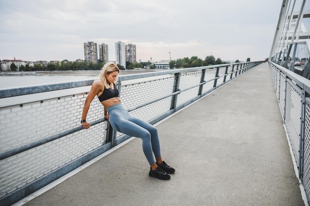 Fitte junge Frau, die Trizeps-Dip-Übungen macht und sich für das Training auf der Brücke in der Stadt aufwärmt.