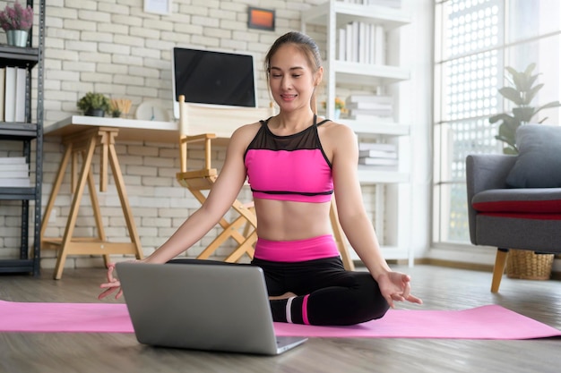 Fitte junge Frau, die zu Hause Yoga über einen Online-Kurs mit einem professionellen Lehrer praktiziert