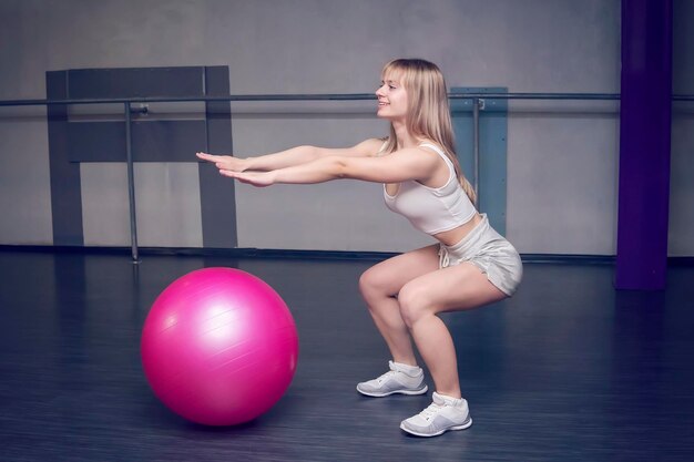 Fitte junge hübsche Frau, die Kniebeugen-Übungen mit Fitness-Ball-Seitenansicht macht