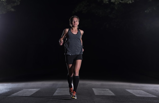 Fitte muskulöse Läuferin, die nachts auf einer schönen Straße in der Natur für den Marathonlauf trainiert.