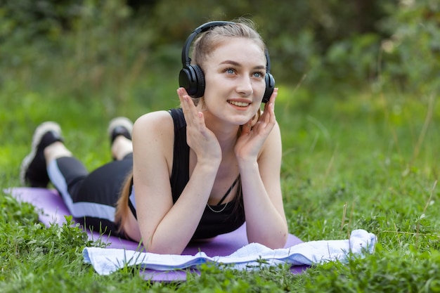Fitte schlanke Frau liegt auf der Matte und hört im Park Musik über Kopfhörer Gesunder Lebensstil