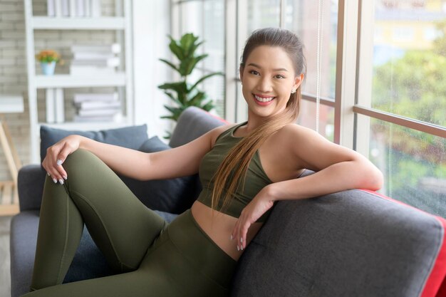 Fitte schöne Frau in Sportkleidung, die nach dem Training auf dem Sofa sitzt und sich entspannt