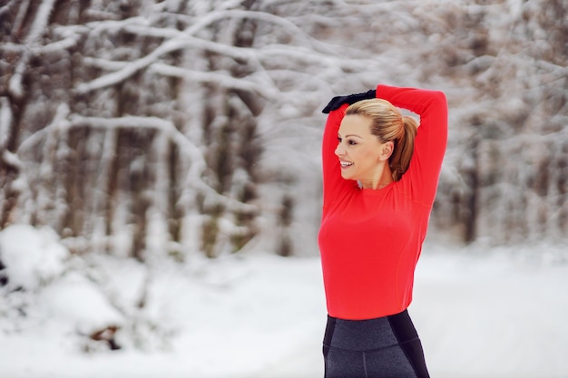 Fitte Sportlerin, die am verschneiten Wintertag in der Natur steht und Aufwärm- und Dehnungsübungen macht. Gesundes Leben, Aufwärmübungen, Winterfitness