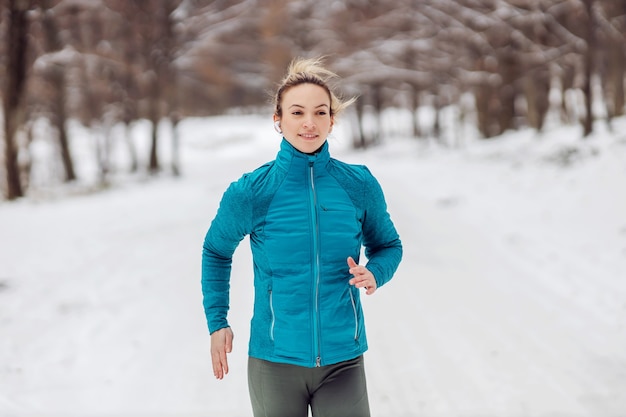 Fitte Sportlerin, die auf einem verschneiten Weg in der Natur läuft. Kaltes Wetter, Schnee, gesundes Leben, Fitness