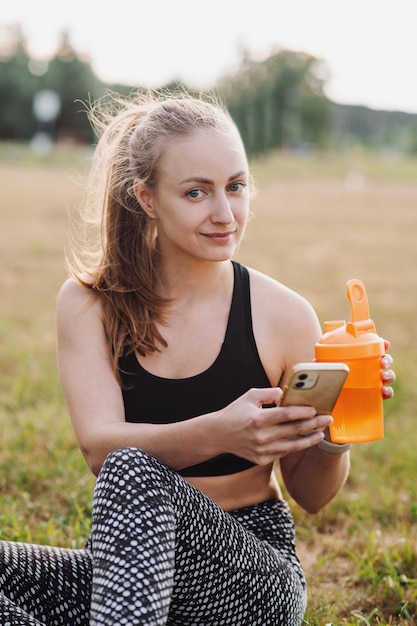 Fitte sportliche Frau mit Wasserflasche entspannt sich nach dem Training im Freien
