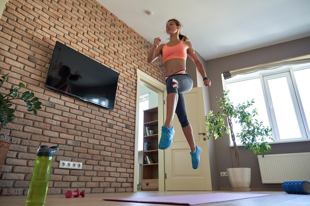 Foto fitte, sportliche junge frau trägt sportkleidung und macht zu hause fitness-sprungübungen