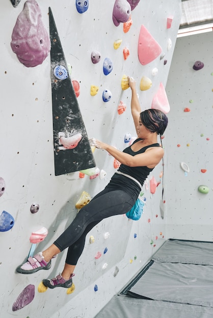 Fitte, starke junge Frau, die ohne automatische Sicherungsgeräte an einer Boulderwand klettert