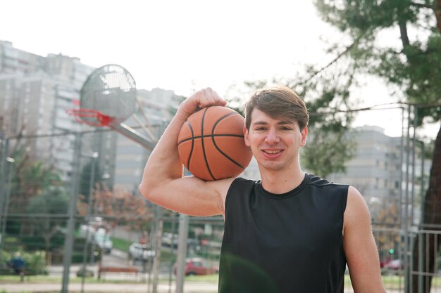 Fitter junger Mann in Sportbekleidung, der die starke Geste mit einem Basketball auf einem Basketballplatz macht