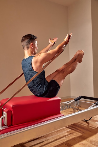 Fitter Mann, der eine Longe-Stretch-Yoga-Pilates-Übung macht, um seine Muskeln mit einem Reformer in einem Fitnessstudio zu stärken und zu straffen