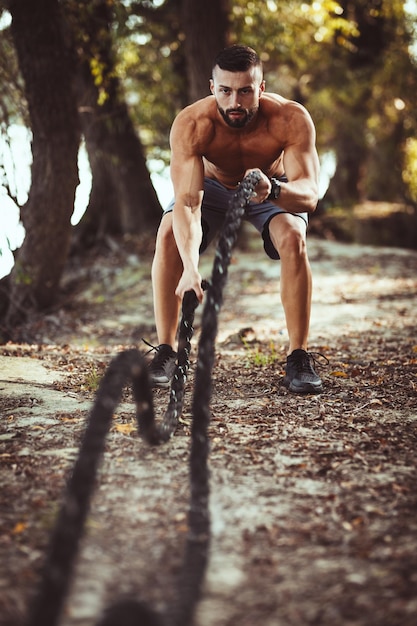 Fitter muskulöser junger Mann macht Übungen mit Seilen in der Natur.