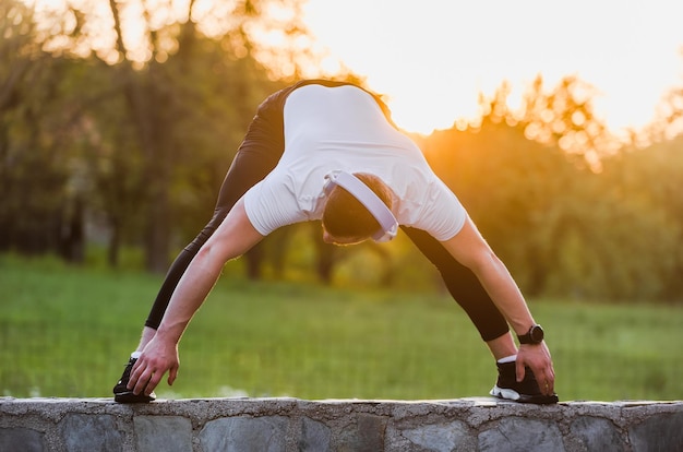 Fitter Sportler, der Musik hört, während er Dehnübungen macht, bevor er im Freien läuft oder trainiert