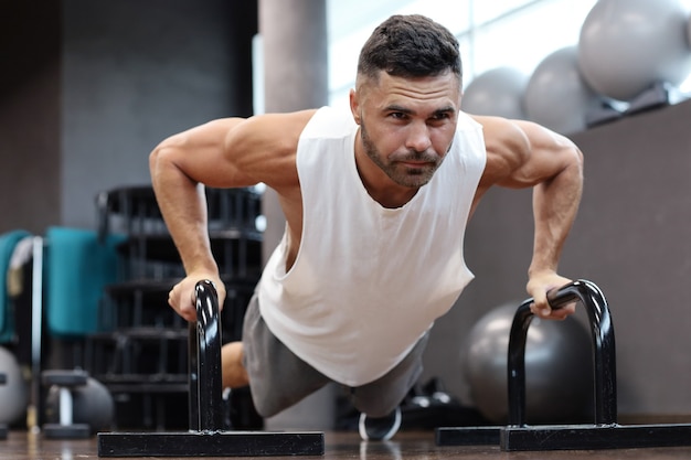 Fitter und muskulöser Mann, der horizontale Liegestütze mit Stangen im Fitnessstudio macht.