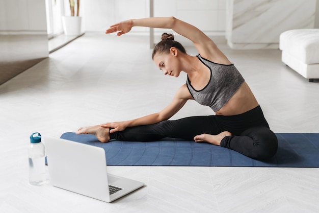 Fittes sportliches Mädchen, das zu Hause Yoga mit Laptop praktiziert