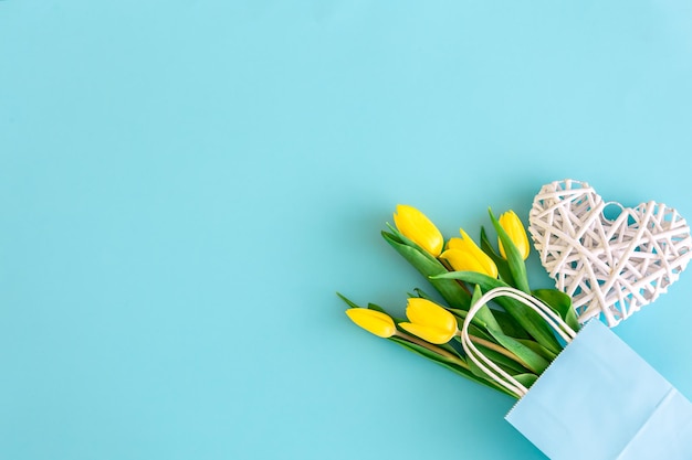 Flach blauer Hintergrund mit gelben Tulpenblumen in einer Papiertüte