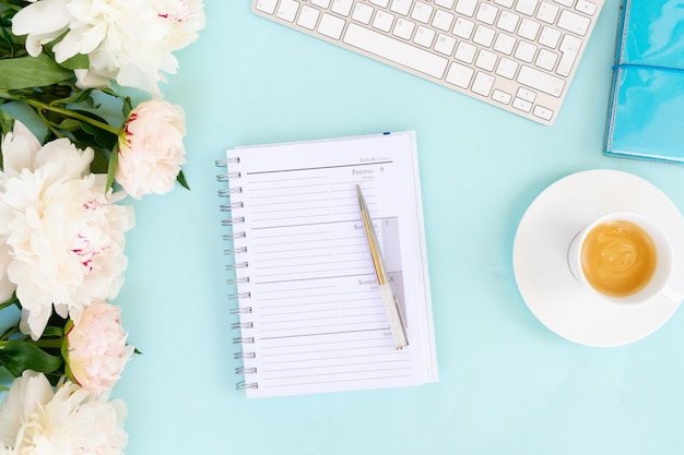 Flach gelegener Büroraum mit leerem Notebook, Tastatur, Pfingstblumen und einer Tasse Kaffee