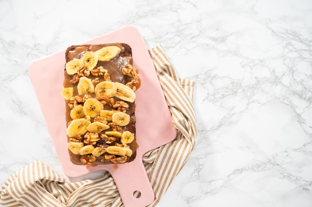 Flach liegen. Backt frisch einen Laib Bananen-Nuss-Brot mit hausgemachtem Karamell auf einem rosa Schneidebrett.