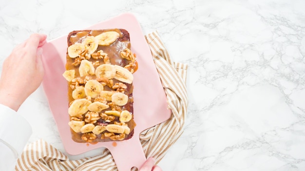 Flach liegen. Bananen-Nuss-Brot in Scheiben schneiden, mit Karamell garnieren und mit Bananenchips und Walnüssen garnieren.