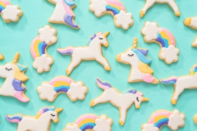 Flach liegen. Einhorn-Zuckerplätzchen verziert mit königlicher Zuckerglasur und Lebensmittelglitter auf blauem Hintergrund.