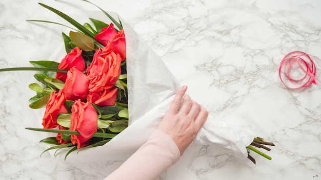 Flach liegen. Florist, der rote Rosen in einen schönen Blumenstrauß einwickelt.