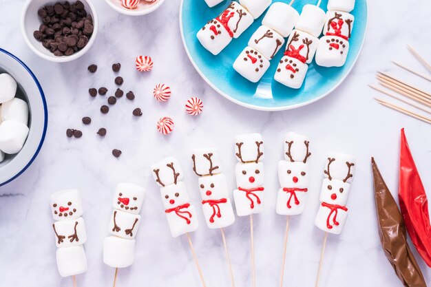 Flach liegen. Marshmallow-Schneemänner und Rentiere auf Stäbchen für heiße Schokolade und Kakaogetränke herstellen.