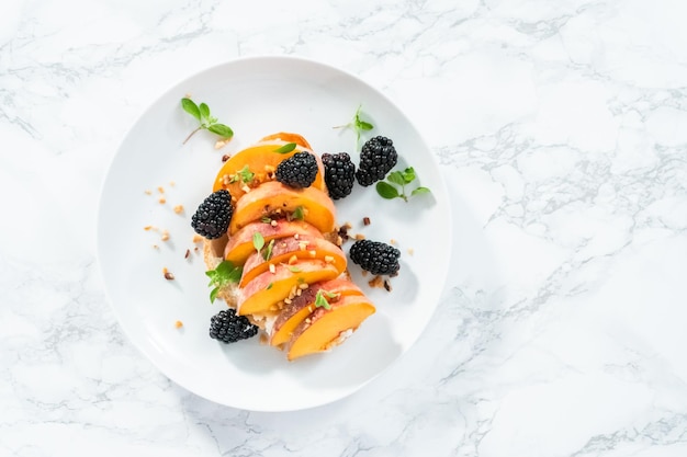 Flach liegen. Pfirsich-Ricotta-Toast, garniert mit Brombeeren auf einem weißen Teller.