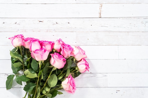 Flach liegen. Rosa Rosen mit dem Stamm auf einem gemalten weißen hölzernen Hintergrund.