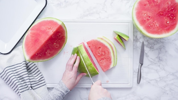 Flach liegen. Rote Wassermelone auf einem weißen Schneidebrett in kleine Stücke schneiden.