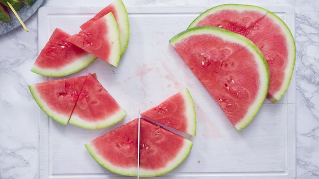 Flach liegen. Rote Wassermelone auf einem weißen Schneidebrett in kleine Stücke schneiden.