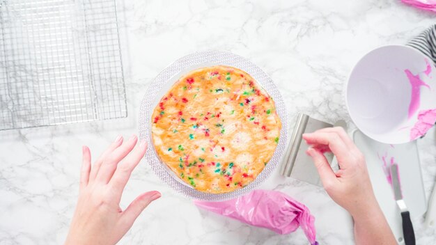 Flach liegen. Schritt für Schritt. Glasieren runder Funfetti-Kuchenschichten mit rosa Buttercreme-Zuckerguss.