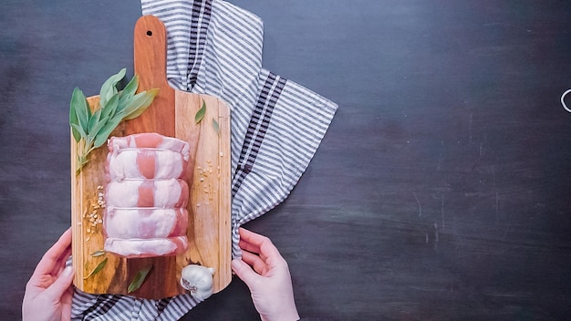 Flach liegen. Schritt für Schritt. Roher Schweinebraten ohne Knochen auf Holzschneidebrett mit Gewürzen.