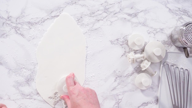 Flach liegen. Schritt für Schritt. Schneeflocken mit Ausstechformen aus weißem Fondant auf einer Marmortheke ausstechen.