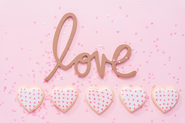 Flach liegen. Zuckerkekse in Herzform, verziert mit königlichem Zuckerguss zum Valentinstag auf rosafarbenem Hintergrund.