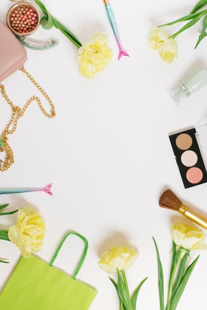 Flache Ansicht von oben Tisch Schreibtischrahmen Femininer Blogger-Schreibtisch-Arbeitsbereich mit Kosmetik-Lippenstift und Tulpenblumen auf weißem Hintergrund