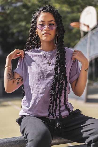 Flache Fokusaufnahme einer afroamerikanischen Frau mit Tätowierungen, die ein lila Hemd und eine Sonnenbrille trägt