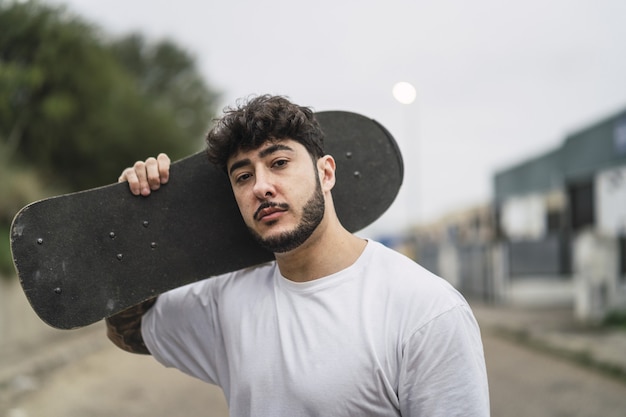 Flache Fokusaufnahme eines gutaussehenden europäischen Skaters, der mit einem Skateboard in den Händen posiert