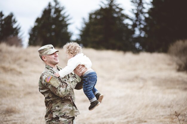 Flache Fokusaufnahme eines lächelnden amerikanischen Soldaten, der sein Baby trägt