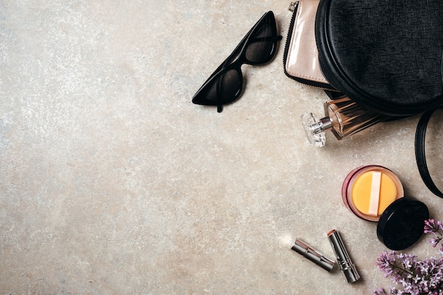 Flache lag moderne minimale Arbeitsbereich Schreibtisch mit Sonnenbrille, Ledertasche, Brieftasche, Frau Kosmetik, Frühling lila Blumen auf Beton Stein Hintergrund.