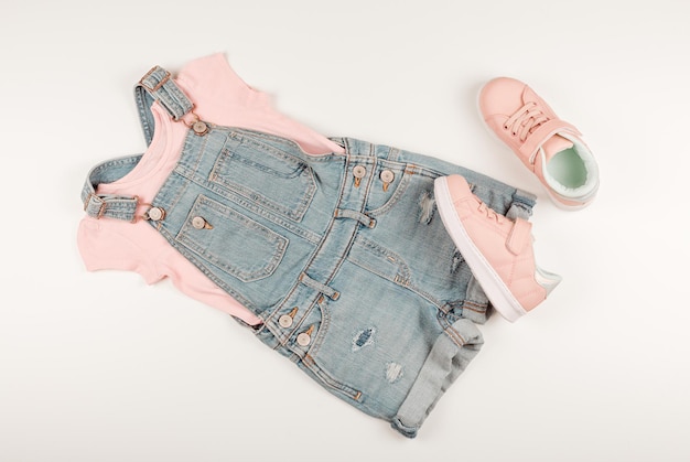 Flache Lage aus rosa T-Shirt, Jeans-Overall und rosa Turnschuhen. Weißer Hintergrund. Babykleidung.