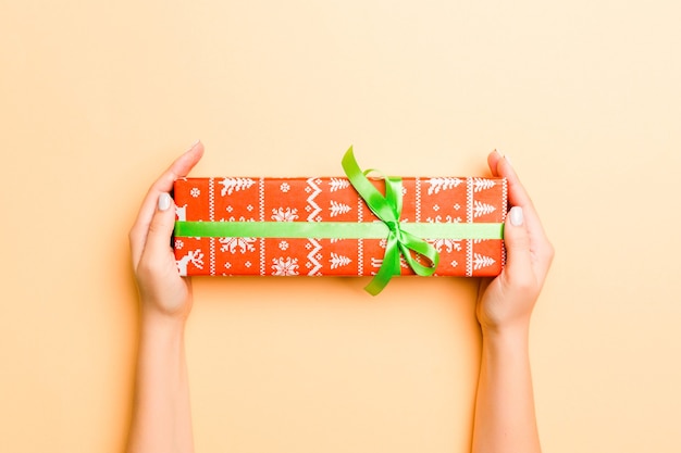 Flache Lage der Frauenhände, die Geschenk verpackt und verziert mit Bogen auf goldenem Hintergrund mit Kopienraum halten. Weihnachts- und Urlaubskonzept.