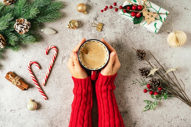 Flache Lage der Frauenhände in rotem Pullover mit Tasse Kaffee Draufsicht auf grauem Hintergrund mit Becher