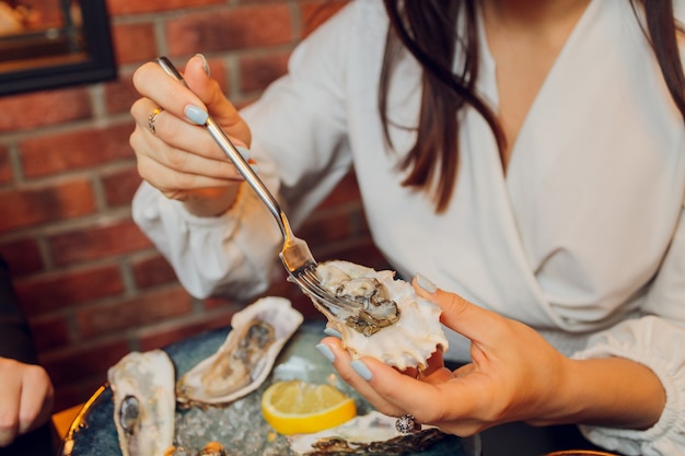 Flache Lage der kaukasischen Hände, die Austern mit anderen Meeresfrüchtegerichten auf einem dunklen Tisch halten.