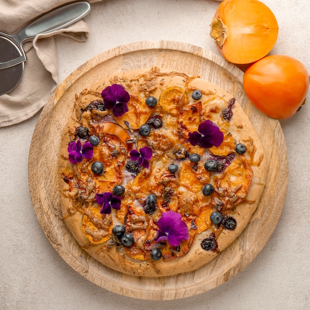 Flache Lage der köstlichen gekochten Pizza mit Kakis und Blütenblättern