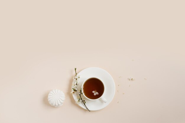 Flache Lage der Teetasse mit Apfelblumen und Marshmallow auf beigem Hintergrund mit Kopierraum