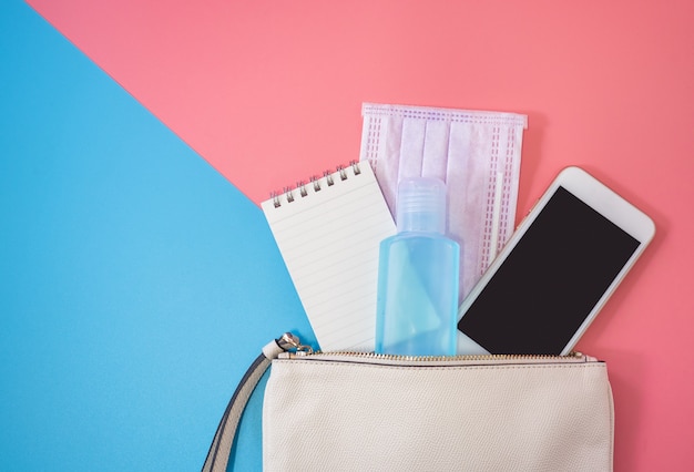 Flache Lage der weißen Ledertasche mit Smartphone und Alkohol-Gel-Desinfektionsmittel auf buntem Hintergrund.