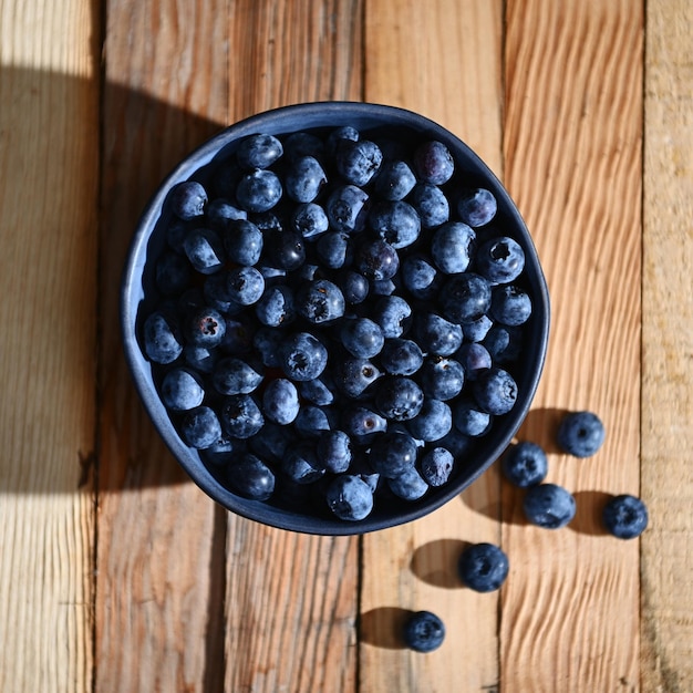 Flache Lage einer blauen Keramikschale voller frischer reifer und verzehrfertiger Bio-Heidelbeeren auf Holzkistenhintergrund